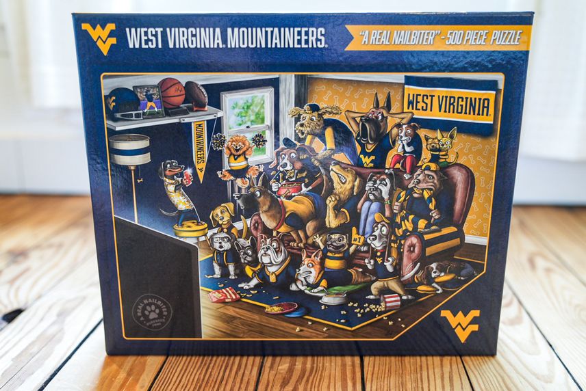 A 500 piece WVU jigsaw puzzle. The puzzle image is of dogs watching a WVU sporting event, surrounded by WVU memorabilia. 
